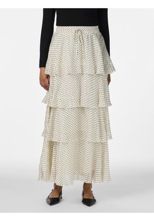 Jupe crème à volants avec pois noirs, taille à cordon, portée avec un haut noir à manches longues et des chaussures noires pointues.