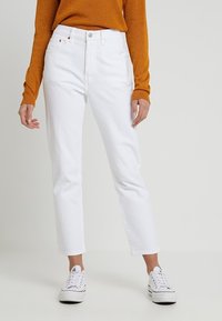 Jeans de mezclilla blanca con corte recto, que presentan una cinturilla estándar, bolsillos frontales y un diseño minimalista. Combinados con un suéter dorado.
