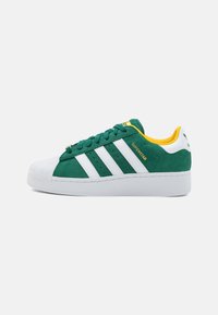 Green suede sneakers with white stripes, rubber sole, and a textured toe cap. Yellow accents on the collar and branding.