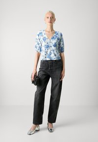 Hvit bluse med blå blomsterdesign, V-hals, puffede ermer; kombinert med svarte high-waisted jeans og sølvfargede block-heel sko.