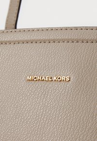 Portefeuille en cuir beige texturé avec des coutures visibles et une plaque logo "MICHAEL KORS" en ton doré.