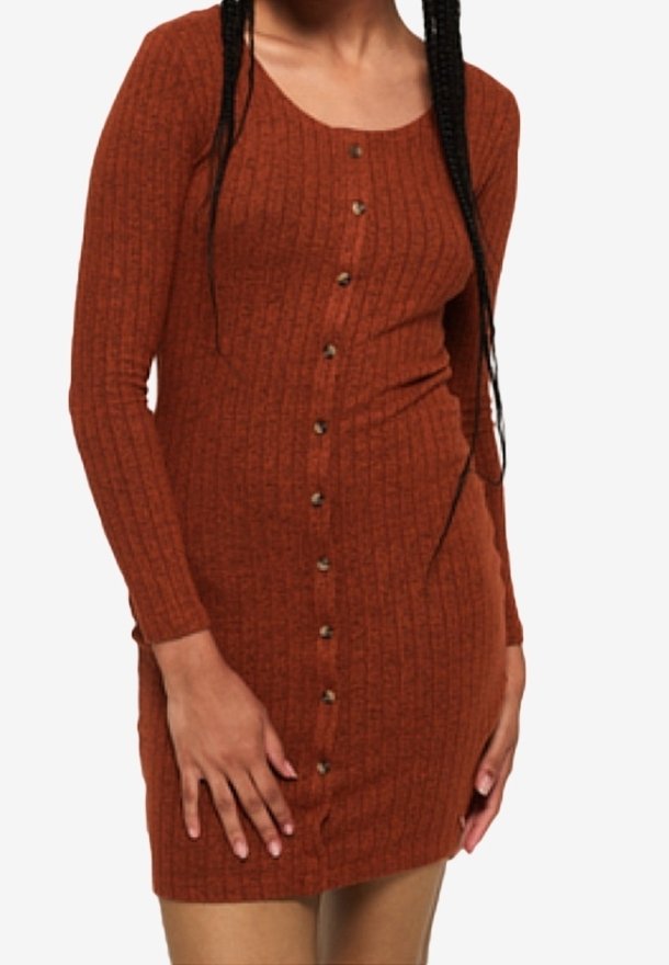 Femme portant une robe boutonnée à manches longues, en côtes, de couleur rouille, avec des boutons sur le devant.