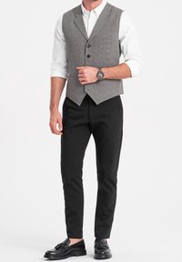 Gråmönstrad väst över en vit skjorta, i kombination med svarta avsmalnande byxor och svarta loafers. Har knappar och en slagkrage-design.