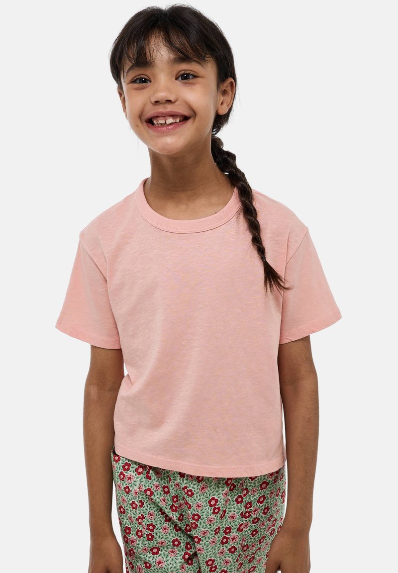 T-shirt rose à manches courtes en tissu doux, avec un col rond et une coupe décontractée, associé à un pantalon vert à imprimé floral.