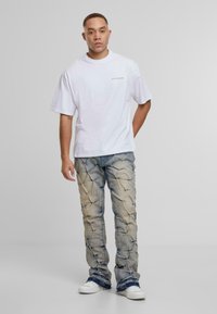 Biała, oversize'owa koszulka z okrągłym dekoltem, zestawiona z jasnoniebieskimi dżinsami o teksturowanym wzorze. Białe trampki dopełniają stylizację.