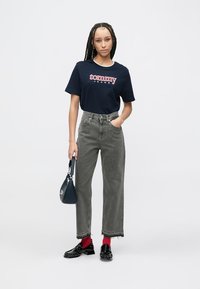 Námornícka bavlnené tričko s logom "tommy", skombinované s vysokými sivými džínsami a čiernymi lakovanými topánkami. Doplnky zahŕňajú malú námornícku kabelku.