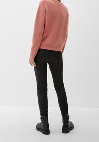Svarta åtsittande byxor och en rosa, texturerad stickad tröja med vid halsringning. Modellen bär svarta ankelstövletter med kraftiga sulor.
