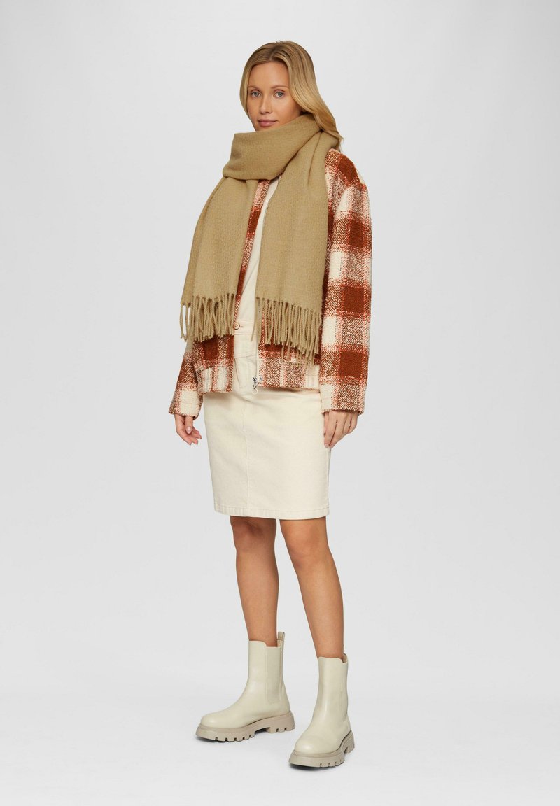 Beige sjaal over een rood-wit geblokte jas, gecombineerd met een crèmekleurige rok en beige enkellaarsjes met dikke zolen.