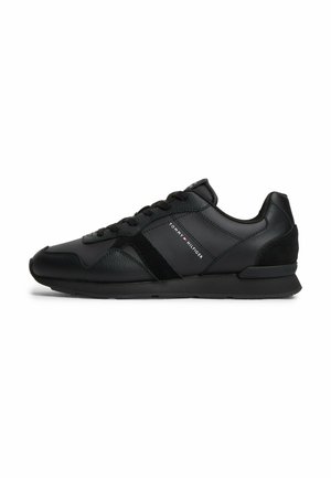 Black low-top sneaker with lace-up front, textured and smooth panels, and "Tommy Hilfiger" logo on the side.
