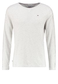 Pitkähihaine, vaalea harmaa paita V-kaula-aukolla, täplikkäällä kankaalla ja vastakkaisella sivustikalla. Sisältää pienen logon rinnassa.