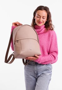 Beige leather backpack with a rounded shape, featuring a front pocket, brown straps, and a small logo on the lower front.
