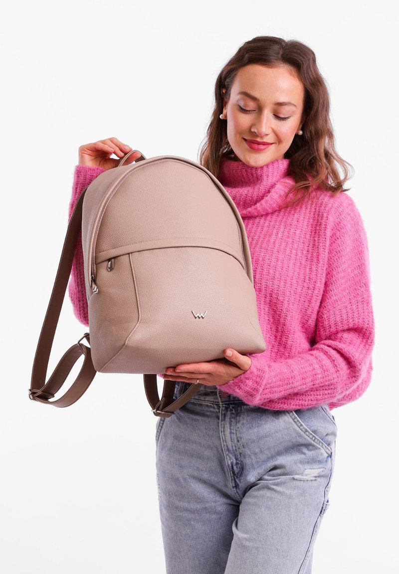 Beige leather backpack with a rounded shape, featuring a front pocket, brown straps, and a small logo on the lower front.