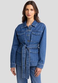 Denim jakna v srednje modri barvi z dolgimi rokavi, pasom, dvema sprednjima žepoma in kontrastnim šivanjem. Strukturiran dizajn z ovratnikom.