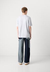 Light gray short-sleeve t-shirt paired with wide-leg denim trousers featuring varying shades of blue and a pocket detail.