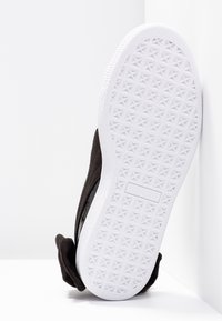 Sneaker nera in suede con una suola in gomma bianca testurizzata. La suola presenta un motivo geometrico a stella e il logo del marchio è impresso di lato.