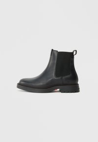 Stivale Chelsea in pelle nera con pannelli laterali elasticizzati, punta tonda, suola in gomma texturizzata e linguetta posteriore per un facile indossamento.