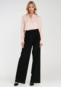 Jasnoróżowa bluzka z długim rękawem i kołnierzykiem, zestawiona z czarnymi, szerokimi spodniami o wysokim stanie i czarnymi szpilkami.