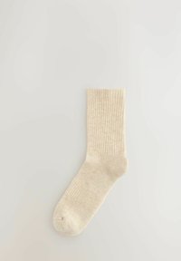 Beige geribbelde sok met een zachte textuur, voorzien van een ronde teen en een boord die tot halverwege de kuit reikt.