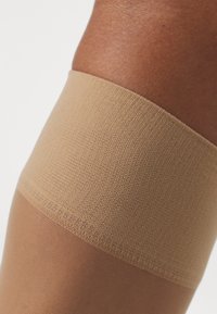 Beiga strumpor som går upp till låret, med ett texturerat övre band, slät underdel och en subtil lyster, designade för komfort och passform.