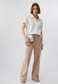 Chemise légère à manches courtes avec une poche poitrine, associée à un pantalon beige texturé avec des motifs subtils. Accessoires : une pochette argentée.