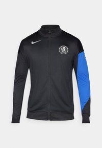 Black zippered jacket with black body and blue sleeve. Features Nike logo and FC emblem, made from lightweight, smooth fabric.