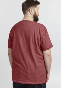 Rød t-shirt med korte ærmer i et let, struktureret stof med rund hals og et lille logo mærke ved kanten. Enkel design uden mønstre.