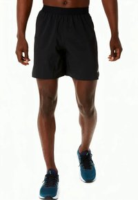 Crne atletske šorceve s elastičnim pojasom, dužine do sredine butina, glatke teksture, upareni s teget tenisicama za trčanje s crnim detaljima.