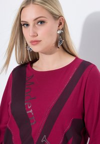 Bordeauxfarbene Baumwoll-T-Shirt mit dem grafischen Text "Modern" in metallischer Druckoptik, verziert mit dekorativen Strasssteinen und einem runden Halsausschnitt.