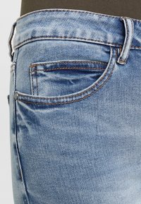Jeans de mezclilla de lavado claro con un bolsillo trasero, costuras en contraste y una cinturilla. La tela tiene un acabado suave y ligeramente desgastado.