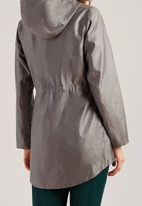 Giacca leggera grigia con cappuccio, vita elastica e maniche lunghe. Presenta una texture liscia e una finitura leggermente lucida.