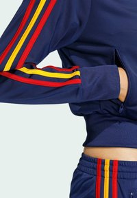 Mornarsko plava dukserica s crvenim i žutim prugama na rukavima, rebrastim manžetnama i džepom sa strane sa patentnim zatvaračem. Glatka tekstura.