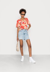 Blusa floral vermelha com mangas curtas, combinada com uma saia mini de denim azul claro. Ténis brancos chunky e uma mala bege completam o visual.