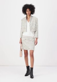 Ensemble de veste et jupe en tweed blanc avec des fils multicolores ; associé à un haut blanc et des bottines noires à talons ; tenant un sac rose pâle.
