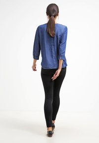 Chemise bleue boutonnée à manches trois-quarts, en tissu doux. Associée à un pantalon skinny noir et des chaussures plates, vue de dos.