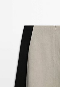 Tweekleurige rok met een gestructureerde lichtgrijze stof aan de ene kant en een effen zwarte stof aan de andere kant, met een centrale ritssluiting aan de achterkant.