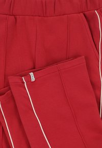 Rode joggingsbroeken van zacht, gestructureerd materiaal met een ontspannen pasvorm. Voorzien van witte piping langs de zijnaad en een elastische tailleband.