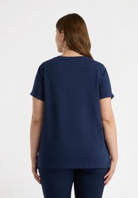 Marineblå kortærmet t-shirt med afslappet pasform, rund hals, rulleærmer og glat tekstur. Bagfra ses et enkelt design uden mønstre.