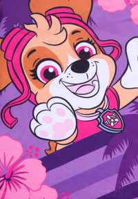 Personaggio di un cane in stile cartone animato con pelliccia marrone, accenti rosa e un'espressione sorridente, vestito con un completo rosa, circondato da motivi floreali viola e rosa.