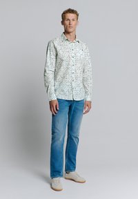 Lange mouwen bloemige shirt in lichtgroen en wit, met knopen en een kraag. Gecombineerd met rechte spijkerbroeken in blauw en beige sneakers.