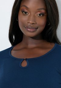 Top azul marino hecho de una tela suave, con detalle de botón en forma de ojo de cerradura en el escote y un diseño de cuello redondo.