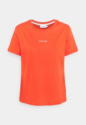 Jasnopomarańczowa koszulka z krótkim rękawem, okrągłym dekoltem i małym białym logo "Calvin Klein" na środku klatki piersiowej.