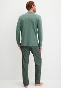 Groene lange mouwen shirt met een ronde hals, gecombineerd met een patroon van donkergroene pyjamabroek met een herhalend geometrisch ontwerp.