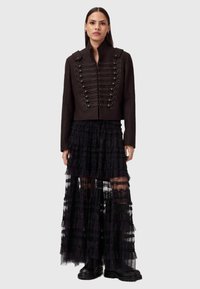 Chaqueta negra corta con un cuello alto y detalles decorativos de lazo, combinada con una falda negra de encaje transparente en capas. Presenta volantes y secciones opacas.