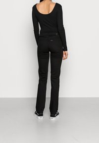 Top negro de manga larga con la espalda descubierta, combinado con pantalones negros ajustados. El modelo lleva zapatillas negras y blancas. Diseño simple y elegante.