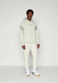 Šviesiai pilkas džemperis su gobtuvu, ant rankovių juodas logotipas ir užrašai. Derinamas su tokių pačių šviesiai pilkų kelnaičių komplektu ir baltais sportbačiais.