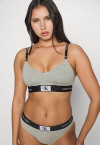 Grå bomull bralette og matchende truser med svarte elastiske bånd som har hvit merkevare. Enkel design, glatt tekstur, og ingen mønstre.
