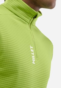 Pull-over rayé vert avec un col zippé, fabriqué à partir d'un tissu léger. Présente un logo de marque blanc bien visible sur le devant.