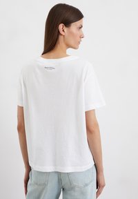 Weißes Baumwoll-T-Shirt mit lockerer Passform, geripptem Rundhalsausschnitt, kurzen Ärmeln und einem dezenten Logo, das auf der Rückseite nahe dem Halsausschnitt gedruckt ist.