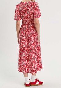 Robe midi fleurie rouge à manches courtes, taille cintrée et jupe fluide. Associée à des baskets rouges et des chaussettes blanches.