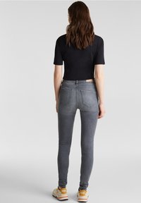 Grå slim jeans med medelhög midja, med bakfickor och en lätt stretch. Kombineras med en svart kortärmad t-shirt och sneakers.